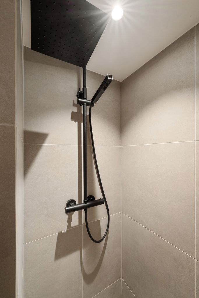 Contemporary shower design featuring sleek black fixtures under soft overhead lighting.