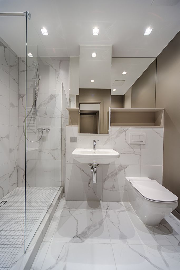 Interior of stylish light bathroom with white sink and toilet and built in shower cabin