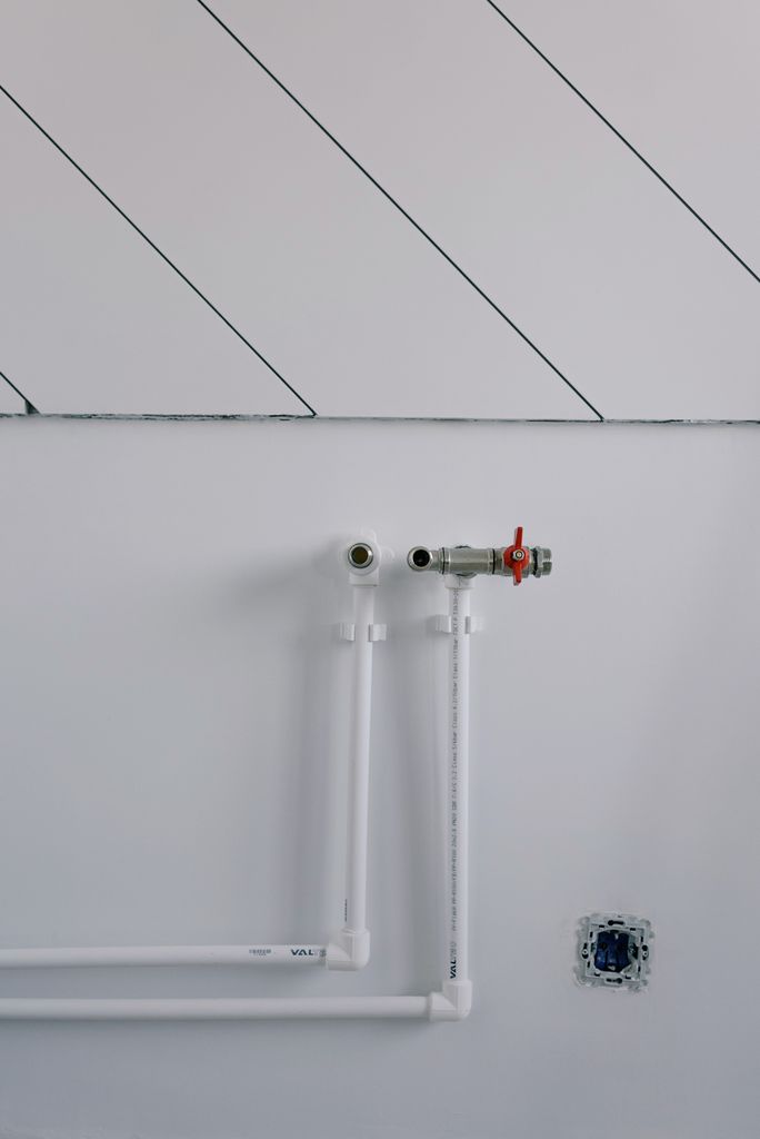 Long thin black slanted lines over pipes of radiator casting shadow on white wall in daytime